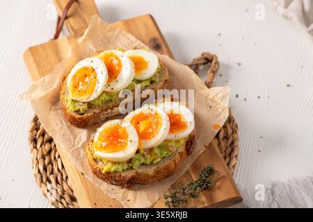 Zwei Scheiben knuspriger Sauerteig, belegt mit Avocadopüree und marmelierten mittelgekochten Eiern. Helles Morgenlicht hebt die Texturen des gewürzten e hervor Stockfoto