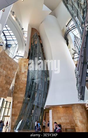 Besucher erkunden das Innere des Guggenheim Museums in Bilbao, Spanien. Das moderne Design zieht die Aufmerksamkeit der Besucher auf sich. Stockfoto