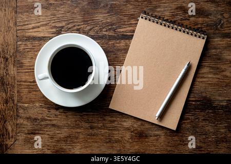 Kaffeetasse und leeres Notizbuch mit Stift auf Holztisch Stockfoto