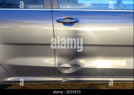 Nahaufnahme einer gebeulten Autotür mit Kratzern und Reflexionen Stockfoto