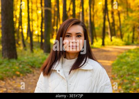 Erfolgreiche Frau posiert in einem herbstlichen Wald. Reife Geschäftsfrau, die einen Spaziergang in der Natur genießt. Porträt einer glücklichen Bloggerin, Mutter und Beruf Stockfoto