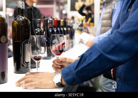 Weinverkostung mit einer Person, die Rotwein im Glas neben verschiedenen Weinflaschen auf einer Weinprobe bei einer Weinveranstaltung schwirbelt Stockfoto