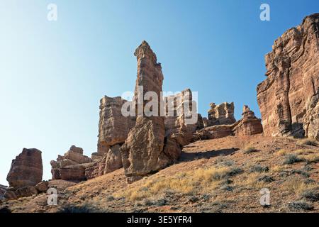 Tiefwinkelaufnahme einer einsamen vertikalen Sandsteinsäule, die sich von einem Wüstenhang inmitten der alten geschichteten Felsformationen des Charyn Canyon Kasachst erhebt Stockfoto