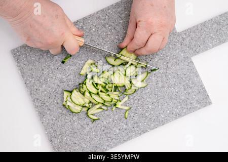 Die Hände einer Frau schneiden eine Gurke auf einem grauen Brett. Stockfoto