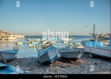 Hurghada, Ägypten, 16. März 2026: Eine Flotte traditioneller Holzfischboote und Skiffs, die auf dem Kieselstrand ruhen und in der ruhigen, blauen Wa schwimmen Stockfoto