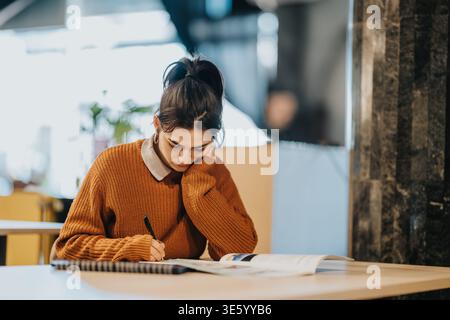 Junge Studentin, die in einem gemütlichen Café studiert und Notizen schreibt, konzentrierte sich auf ihr Notizbuch Stockfoto