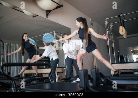 Frau, die ein Pilates-Workout auf Reformer-Maschine mit einem Trainer durchführt, der in einem Studio hilft Stockfoto
