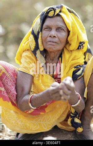 Odisha, Indien - 26. März 2026: Blick auf eine ältere Frau mit gelbem Kopftuch und roten Armreifen, verwitterte Hände, die ein Leben eingeätzt verkörpern Stockfoto