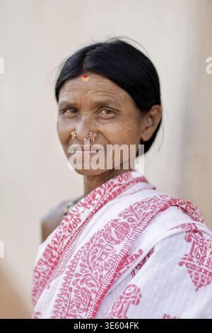 Odisha, Indien - 26. März 2026: Blick auf eine Frau mit alter, verwitterter Haut, die mit einem weißen und roten Sari geschmückt ist, deren Augen eine lebenslange Geschichte widerspiegeln. Stockfoto