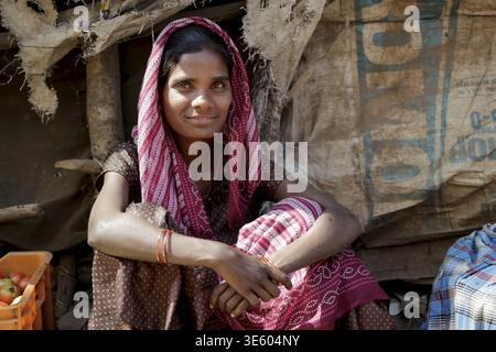 Odisha, Indien - 26. März 2026: Blick auf eine Frau mit einem rot-weiß gemusterten Schal, deren Augen das sanfte Licht reflektieren, vor einem Makeshi sitzend Stockfoto