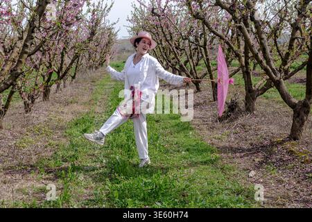 Frau tanzt fröhlich mit rosa Sonnenschirm im blühenden Obstgarten Stockfoto