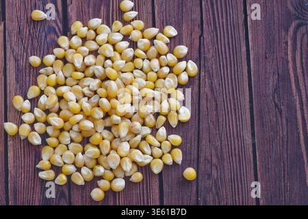 Popcorn-Kerne verteilen sich auf einer Holzoberfläche und betonen die natürliche Textur und den rustikalen Charme. Ideal für Konzepte wie Snack Food, Kochen, Kino, Stockfoto