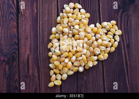 Popcorn-Kerne verteilen sich auf einer Holzoberfläche und betonen die natürliche Textur und den rustikalen Charme. Ideal für Konzepte wie Snack Food, Kochen, Kino, Stockfoto