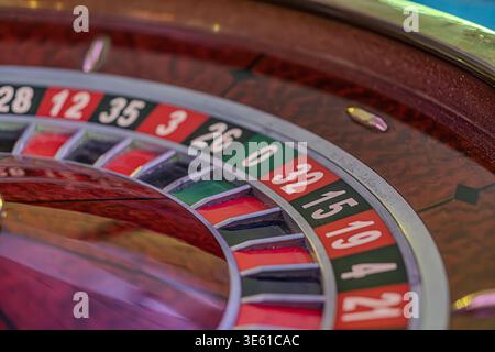 Nahaufnahme eines schwach beleuchteten Casino-Innenraums mit einem hell beleuchteten Roulette-Rad mit wechselnden roten und schwarzen Segmenten, nummeriert von 1 bis 36 Stockfoto