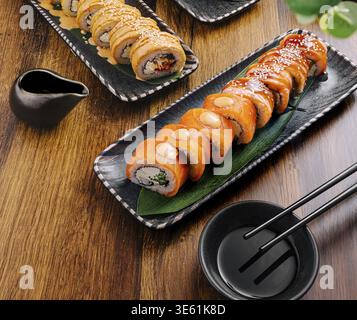 Das Essen, die köstlichen Sushi-Brötchen sind wunderschön auf schwarzen Tellern angeordnet, mit lebhaften Farben und einer Vielzahl von Zutaten. Sojasauce und Essstäbchen Stockfoto