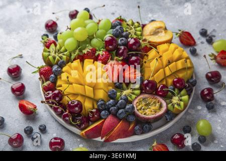 Essen, köstliche Obst- und Beerenplatte. Mango, Kiwi, Erdbeere, Traube, Kirsche, Heidelbeere, Pfirsich und Passionsfrucht, selektiver Fokus Stockfoto