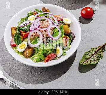 Essen, Eine bunte Salatschale mit frischem Gemüse, Kirschtomaten, Radieschen, gekochten Eiern und Thunfisch, kunstvoll auf einer strukturierten Oberfläche angeordnet. T Stockfoto