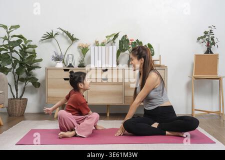 Eine Mutter und ihre Tochter teilen Lachen und Verbundenheit, während sie Dehnübungen auf ihren Yogamatten üben, um Gesundheit und Beziehungsfähigkeit zu fördern Stockfoto