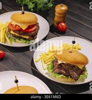 Speisen, verschiedene Gourmet-Burger, begleitet von knusprigen Pommes frites, werden auf einfachen Tellern serviert. Die Einrichtung verfügt über einen rustikalen Holztisch und frisches Gemüse Stockfoto