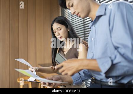 Eine Geschäftsfrau und ein Geschäftsmann prüfen Dokumente und diskutieren Projektdetails in einer stilvollen, modernen Büroumgebung Stockfoto