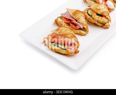 Speisen, frisch gebackene Croissants gefüllt mit Lachsscheiben, Schinken und Gurken ruhen auf einer weißen Servierplatte, perfekt für einen Brunch oder Snack Stockfoto