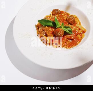 Essen, Ein Teller bietet eine Portion Pasta mit herzhaften Fleischbällchen, reichhaltiger Tomatensauce und frischem Basilikum. Der weiße Hintergrund betont das leuchtende c Stockfoto