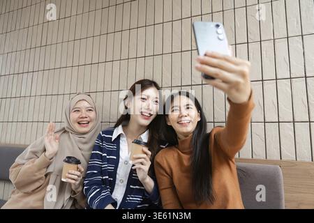 Eine Gruppe von Freunden macht ein fröhliches Selfie in einem Café, in dem sie ihre Verbundenheit hervorheben und spielerische Momente bei einem Kaffee teilen. Dabei werden Jugendliche und Verbundenheit begrüßt Stockfoto