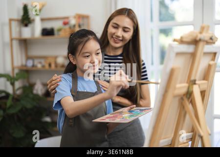 Eine fröhliche Mutter und Tochter, die eine Maltätigkeit ausüben, Kreativität und Verbundenheit zum Ausdruck bringen, während sie zu Hause Spaß haben Stockfoto
