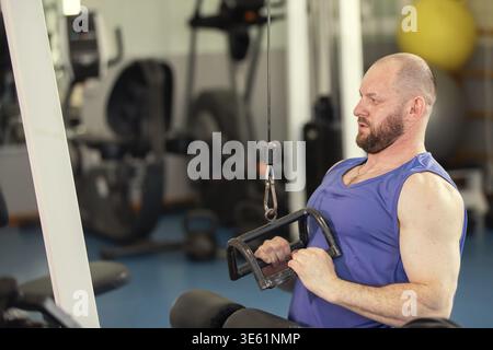 Ein männlicher Athlet trainiert auf einem Krafttraining-Gerät in einem Fitnessstudio. Er konzentriert sich auf die Übung Stockfoto