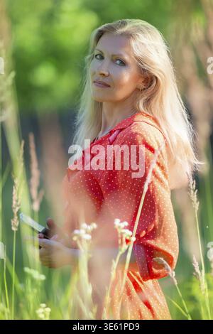 Vertikales Porträt einer schönen blonden Frau mittleren Alters im grünen Gras Stockfoto