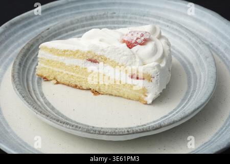 Ein kleiner japanischer Erdbeerkuchen auf zwei stilvollen überlappenden großen und kleinen Tellern im japanischen Stil auf einem schwarzen Tuch auf einem weißen Tisch Stockfoto