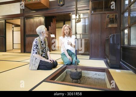 Zwei Frauen sitzen auf dem Boden in einem Raum im japanischen Stil. Eine der Frauen zeigt auf etwas Stockfoto