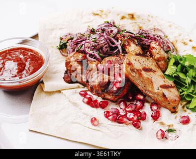 Speisen, saftiges gegrilltes Fleisch wird auf einem Fladenbrot präsentiert, begleitet von Granatapfelkernen, frischen Kräutern und dünn geschnittenen Zwiebeln, was ein lebendiges an liefert Stockfoto