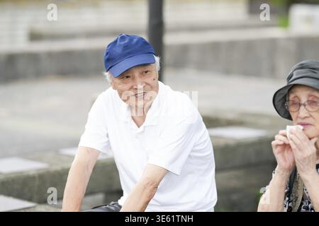 Ein älterer Mann mit blauem Hut und weißem Hemd sitzt auf einer Bank. Eine Frau mit Hut und Brille sitzt neben ihm Stockfoto