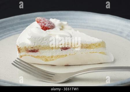 Ein kleiner japanischer Erdbeer-Shortcake und je eine Gabel auf zwei stilvollen, großen und kleinen Tellern im japanischen Stil auf einem schwarzen Tuch auf einem weißen Tisch Stockfoto