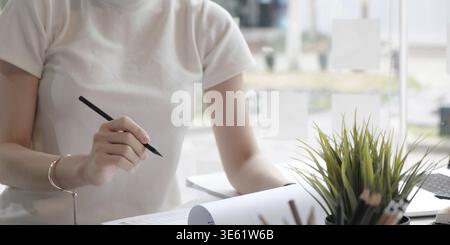Großaufnahme asiatische Frau, die auf Notizbuch auf Tisch mit Laptop schreibt, Mädchen arbeiten im Café, freischaffendes Geschäftskonzept Stockfoto