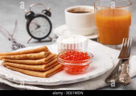 Frühstück. Dünne Pfannkuchen mit rotem Kaviar in weißer Schüssel auf dem Tisch. Crepes. Kaffee und Saft. Selektiver Fokus Stockfoto