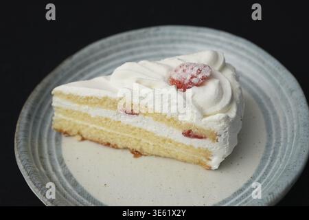 Ein kleiner japanischer Erdbeerkuchen auf einem stilvollen japanischen Teller auf einem schwarzen Tuch auf einem weißen Tisch Stockfoto