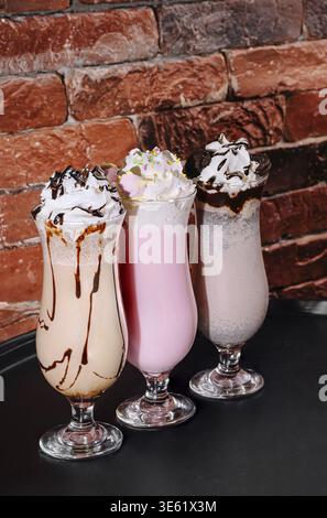 Essen, drei bunte Milchshakes werden in eleganten Gläsern serviert, jeder mit Schlagsahne belegt und mit Schokolade getränkt. Sie werden dagegen dargestellt Stockfoto