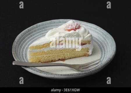 Ein kleiner japanischer Erdbeer-Shortcake und eine kleine Gabel auf einem stilvollen japanischen Teller auf einem schwarzen Tuch auf einem weißen Tisch Stockfoto