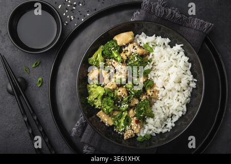Essen, Teriyaki-Hühnchen und Brokkoli mit gedämpftem Reis in der Schüssel, Blick von oben, dunkler Hintergrund Stockfoto