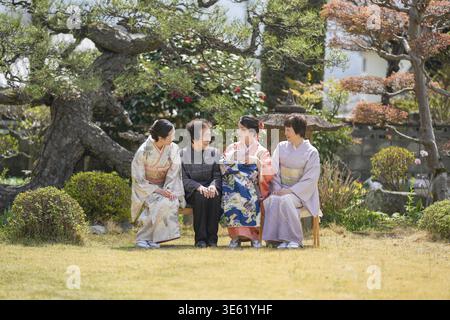 Vier Frauen in traditioneller japanischer Kleidung sitzen auf einer Bank in einem Park. Die Szene ist friedlich und ruhig, während die Frauen sich gegenseitig amüsieren Stockfoto