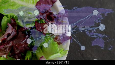 Weiße Salatschale mit rotem und grünem Salat auf dunkler Tischplatte mit holografischer Kartenüberlagerung Stockfoto