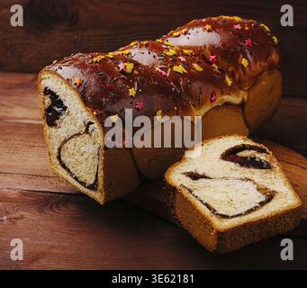 Essen, Ein frischer Brotlaib gefüllt mit reichhaltiger Schokolade, gekrönt mit lebhaften Streuseln, wird auf einem Holzbrett platziert. Ein geschnittenes Stück zeigt das d Stockfoto