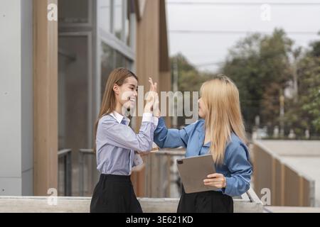 Zwei verschiedene Frauen feiern ihren Erfolg mit einem High-Five, während sie ein Tablet im Freien halten und dabei Freude und Teamarbeit zum Ausdruck bringen Stockfoto