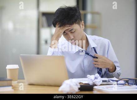 Ein Geschäftsmann oder Büroangestellter spürt Überlastung und Stress, zieht an seiner Krawatte, während er auf seinen Laptop blickt und möglicherweise mit dem Bus zu tun hat Stockfoto