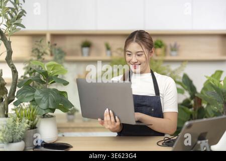 Eine freudige Frau greift in einem belebten Innengarten mit ihrem Laptop in Berührung und reflektiert die Zukunft der Arbeit und ein positives Arbeitsumfeld Stockfoto
