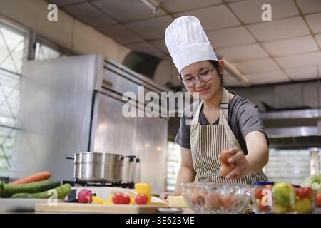 Nahaufnahme eines Küchenchefs, der braune Eier aus einer Glasschale auf einer Küchentheke auswählt, umgeben von frischem Obst und Gemüse Stockfoto