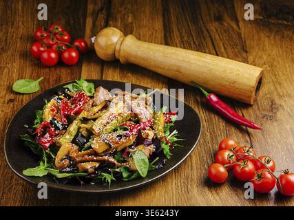 In einem schwarzen Gericht wird Ein lebendiger Pfannenbraten mit verschiedenen Gemüsesorten wie Auberginen, Paprika und Gemüse serviert. Frische Kirschtomaten und A Stockfoto