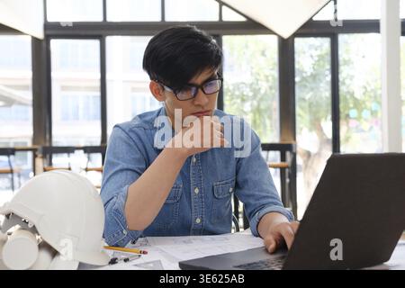 Ein fokussierter Architekt und Ingenieur, der mit einem Laptop an Bauplänen arbeitet. Sie konzentrieren sich auf Konstruktion und Planung und arbeiten an präzisen und d Stockfoto